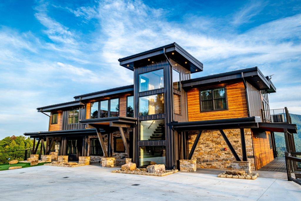 Modern timber-and-stone cabin exterior photographed beneath a blue mountain sky.
