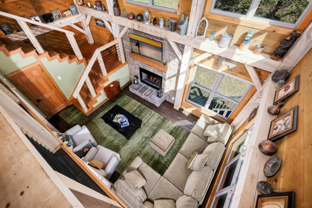 Overhead loft view of a timber-frame great room and stone fireplace.